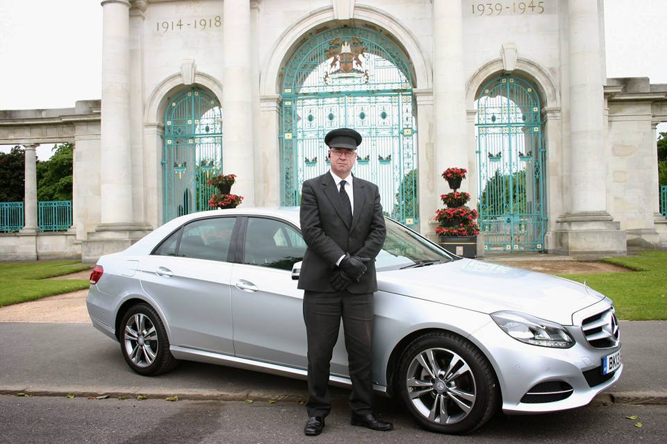 Uniformed Derby Chauffeurs VIP chauffeur standing beside a silver Mercedes E-Class