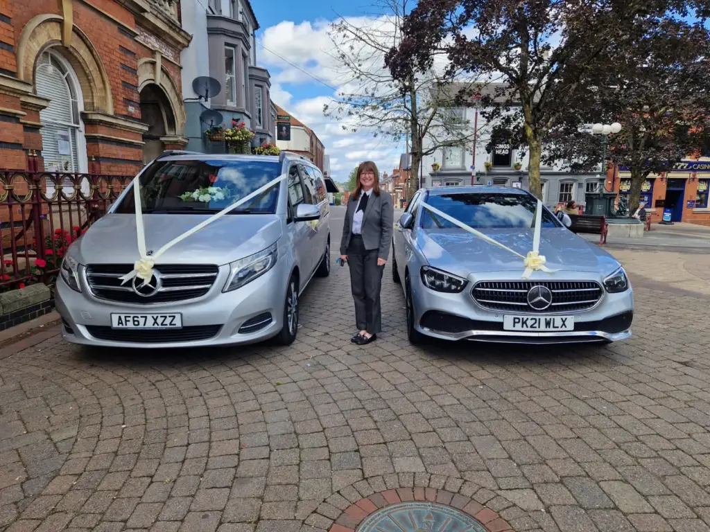 A chauffeur standing between a silver Mercedes V-Class and E-Class dressed with ribbons
