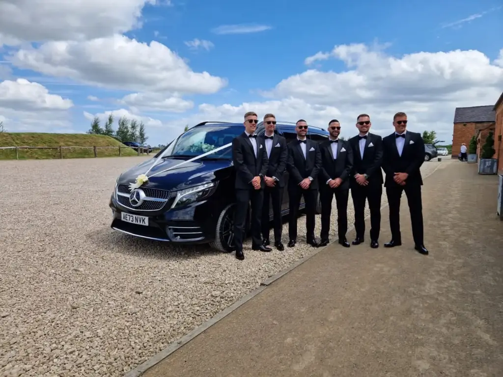 A black Mercedes V-Class dressed in wedding ribbons with six ushers in black tie